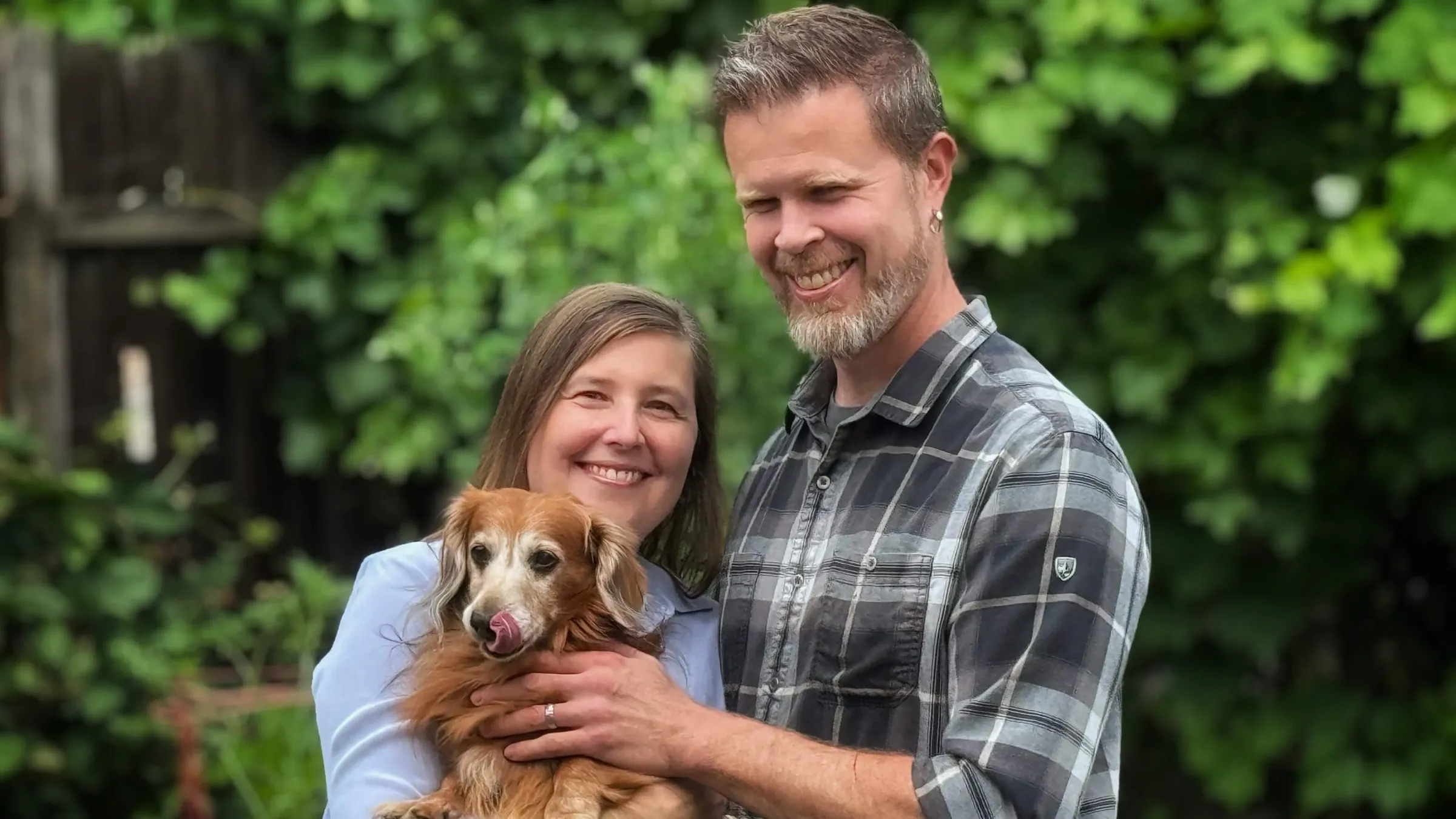 Kimiya's two founders smiling in a garden, holding their long-haired dachshund.